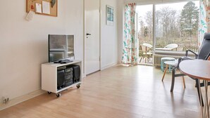 A room with a television on a cart, a dining table with chairs, a door, and a view of the outdoors. - 2 Person Holiday Home in Aakirkeby (Akirkeby)
