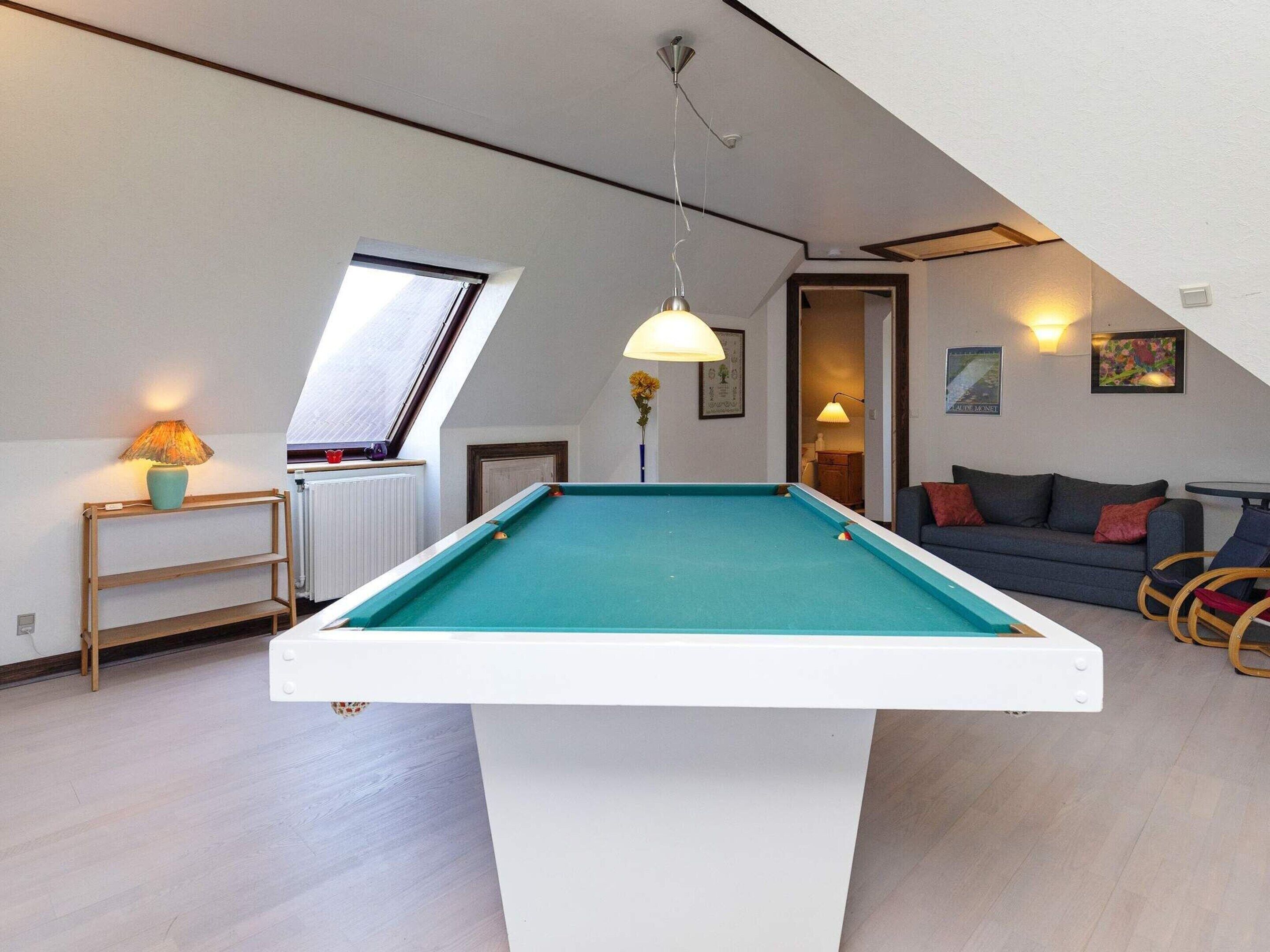 A pool table in a room with a sloped ceiling, a sofa, a lamp, and a radiator.
