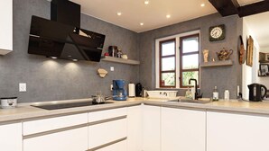 A modern kitchen with white cabinets, a black range hood, a coffee maker, and a window with a view of greenery. - 12 Person Holiday Home in Idestrup (Idestrup)