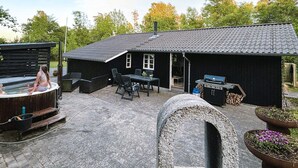 Une maison noire avec un toit en tuiles, un jacuzzi, du mobilier d’extérieur et un espace barbecue.