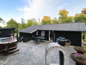 Een zwart huis met pannendak, een bubbelbad, tuinmeubilair en een barbecueplek.
