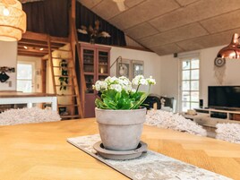 A living room with a wooden table, a grey potted plant, and a television in the background.