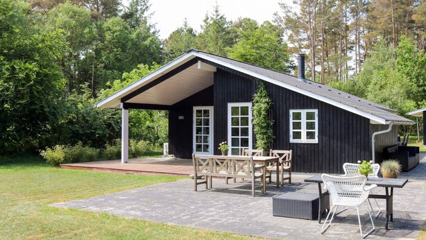 Une maison en bois noire avec un patio couvert, une table et des chaises, et un petit jardin.