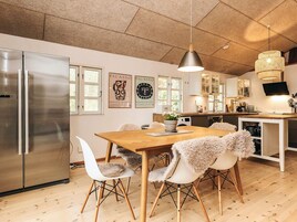 A modern kitchen with a wooden table, white chairs, a stainless steel refrigerator, and artwork on the walls.