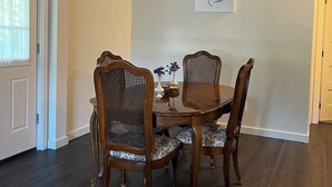 Een eetgedeelte met een ronde tafel en vier stoelen, een lijst met kunstwerk aan de muur, en een deur met een raam.
