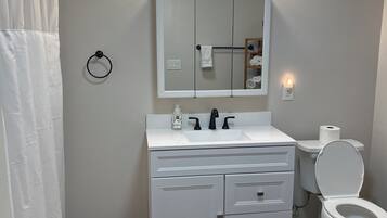 Un baño con tocador blanco, espejo, inodoro y cortina de ducha.