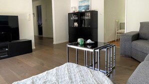 Een moderne woonkamer met een flatscreen televisie, een salontafel met glazen blad, een grijze bank en een zwarte televisiemeubel.