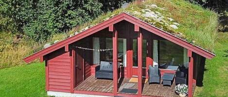 A red wooden cabin with a sloped roof, a porch with outdoor seating, and a small garden area.
