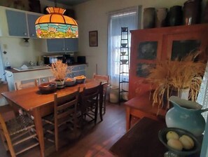 Cozy dining area with a wooden table for four, a stained glass lamp, and a simple kitchen area.