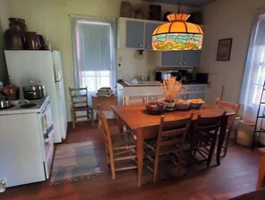 A compact kitchen with a refrigerator, stove, and cabinets. There is a dining table with chairs and a decorative vase.