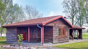 A wooden cabin with a red roof, a porch, and a small garden area.