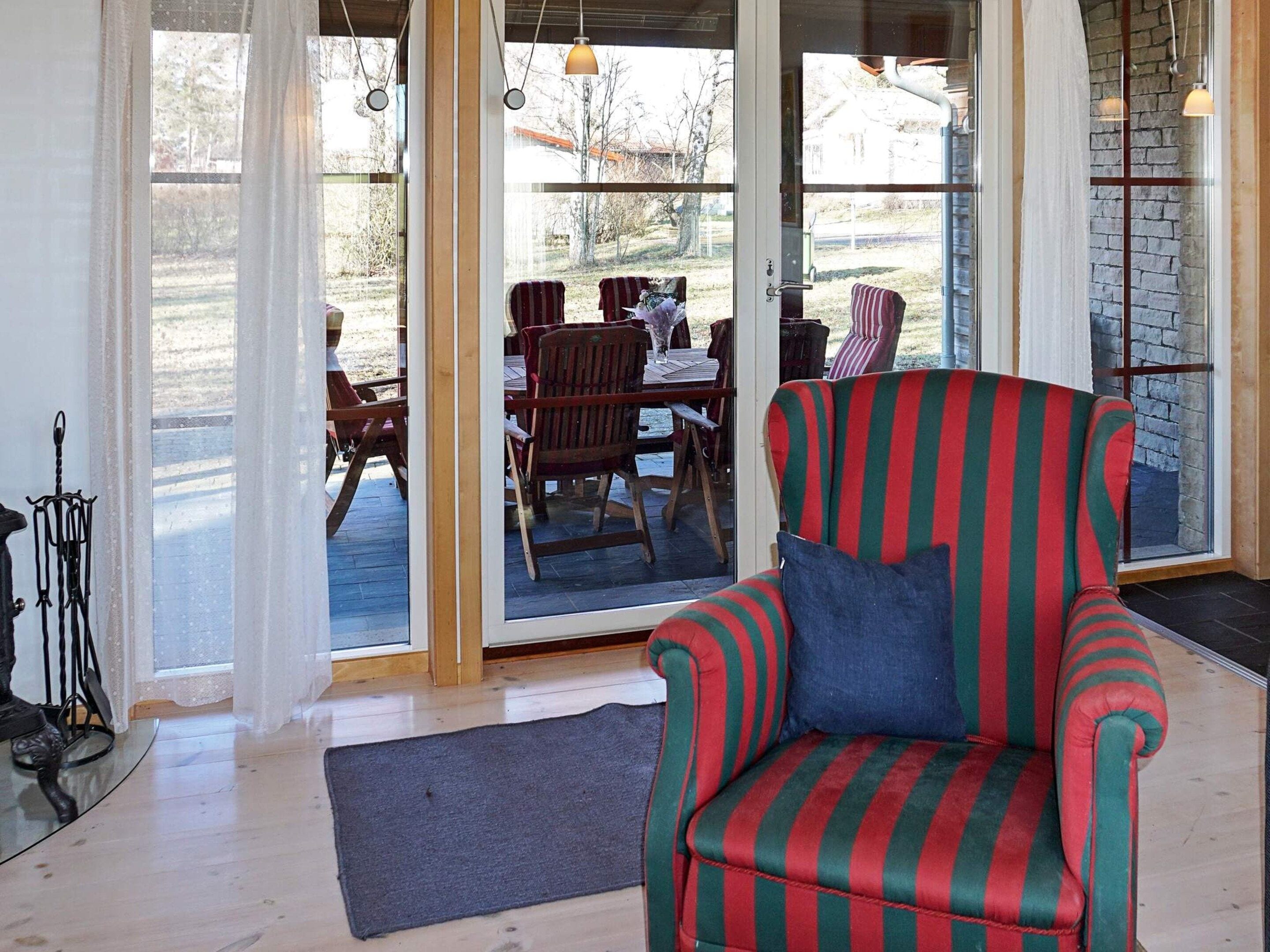 A room with a striped armchair, a wooden dining table with chairs, and a view through glass doors to an outdoor area.