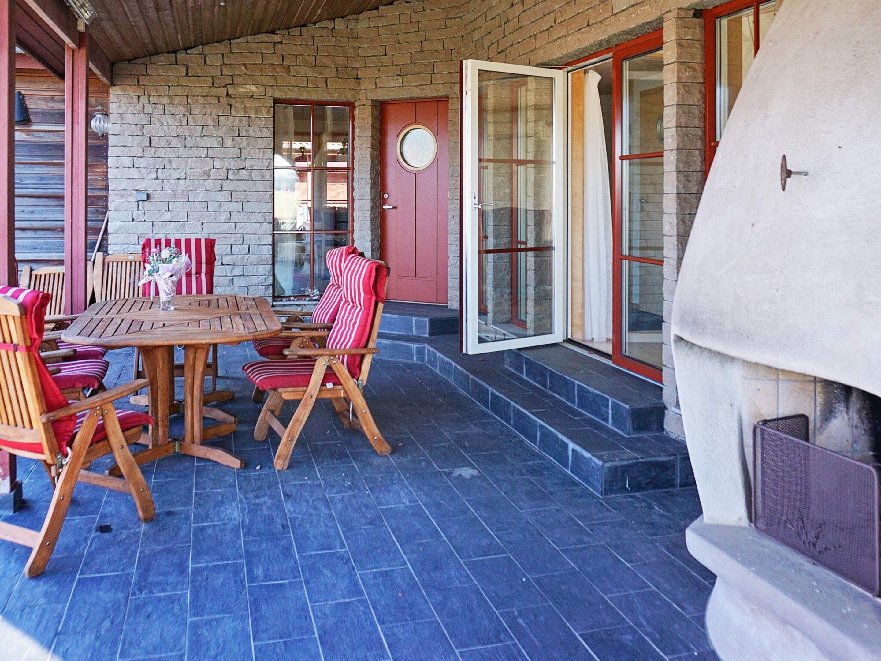 Un patio al aire libre con una mesa y sillas de madera, un muro de ladrillo y un ventanal corredera.