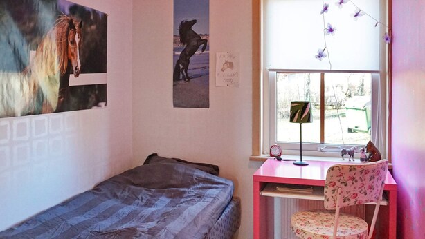 A bedroom with a single bed, a desk with a chair, a window with a view, and a wall with a birthday card.