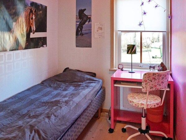 A bedroom with a single bed, a desk with a chair, a window with a view, and a wall with a birthday card.