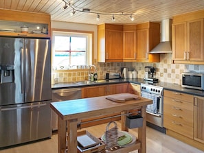 A modern kitchen with stainless steel appliances, wooden cabinets, and a central island with a sink and storage.