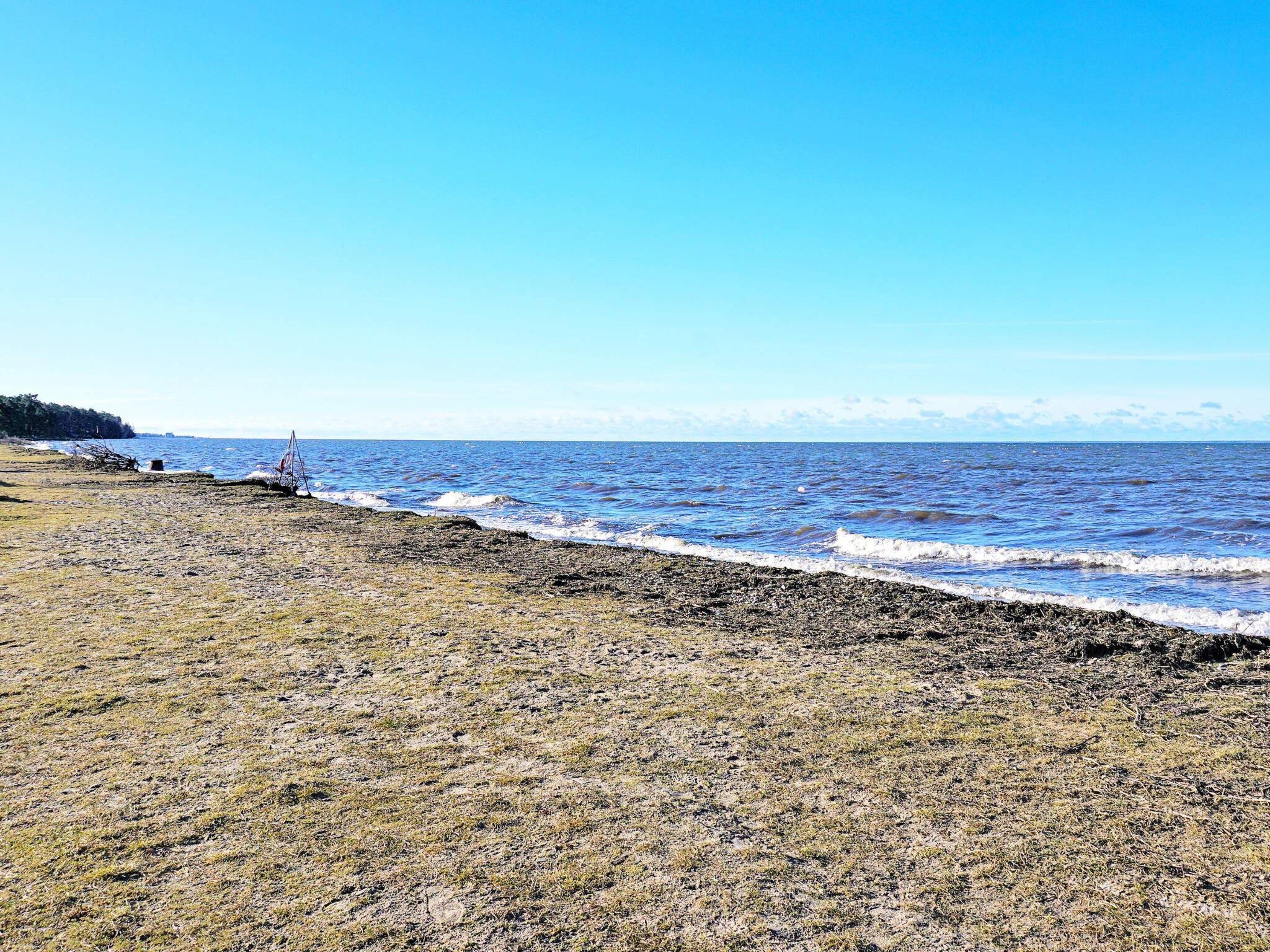 A beach with a clear sky, waves, and a distant shoreline.