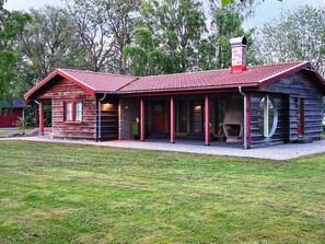 A wooden cabin with a red roof, a porch, and a chimney.