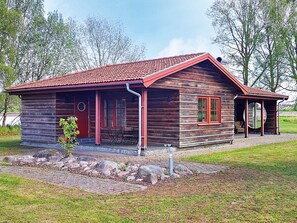 A wooden cabin with a red roof, a porch, and a small garden area. - 4 Star Holiday Home in Morbylanga (Morbylanga)