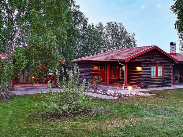 Un chalet rustique avec un toit rouge, entouré d’une végétation luxuriante et d’arbres.