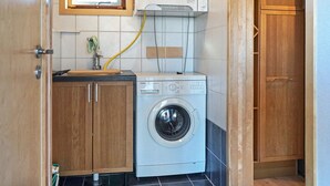 A compact laundry area with a washing machine, wooden cabinets, and a window above the machine.