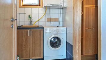A compact laundry area with a washing machine, wooden cabinets, and a window above the machine.