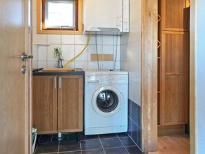 A compact laundry area with a washing machine, wooden cabinets, and a window above the machine.