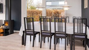 Zona pranzo con tavolo imbandito per sei persone, circondato da sedie, una stufa a legna e due lampade a sospensione.
