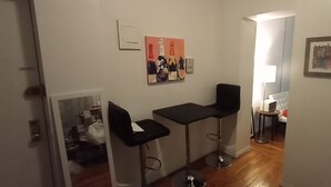 Un couloir étroit avec deux tabourets de bar noirs, une petite table et un tableau accroché au mur.
