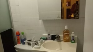 Une petite salle de bain avec des toilettes, un lavabo et un miroir. On trouve des articles de toilette sur le comptoir du lavabo.