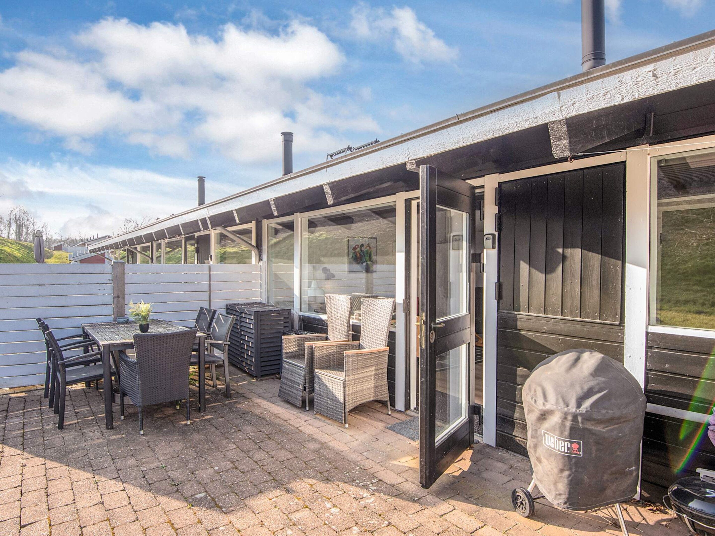 An outdoor patio with a table and chairs, a grill, and a covered area with a Weber logo.