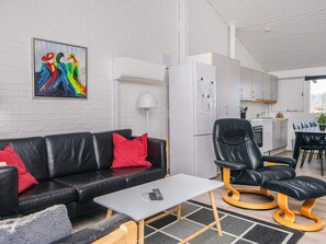 A modern living room with a black leather sofa, a small white table, and a black leather chair. There is a white refrigerator and a kitchen in the background. - 5 Star Holiday Home in Aabenraa (Aabenraa)