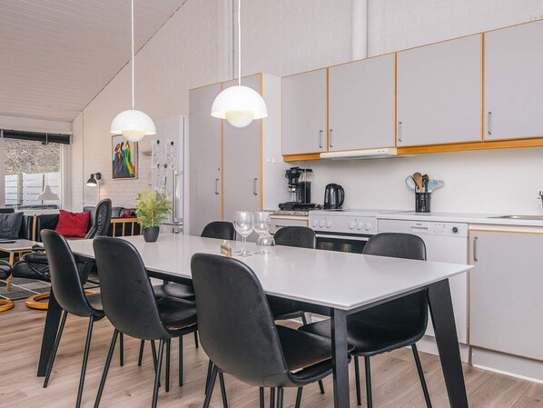 A modern kitchen with white cabinets, a dining table with chairs, and pendant lighting.