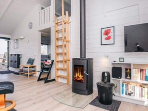 A modern living room with a wood-burning stove, a bookshelf, and a loft bedroom with a ladder. - 5 Star Holiday Home in Aabenraa (Aabenraa)