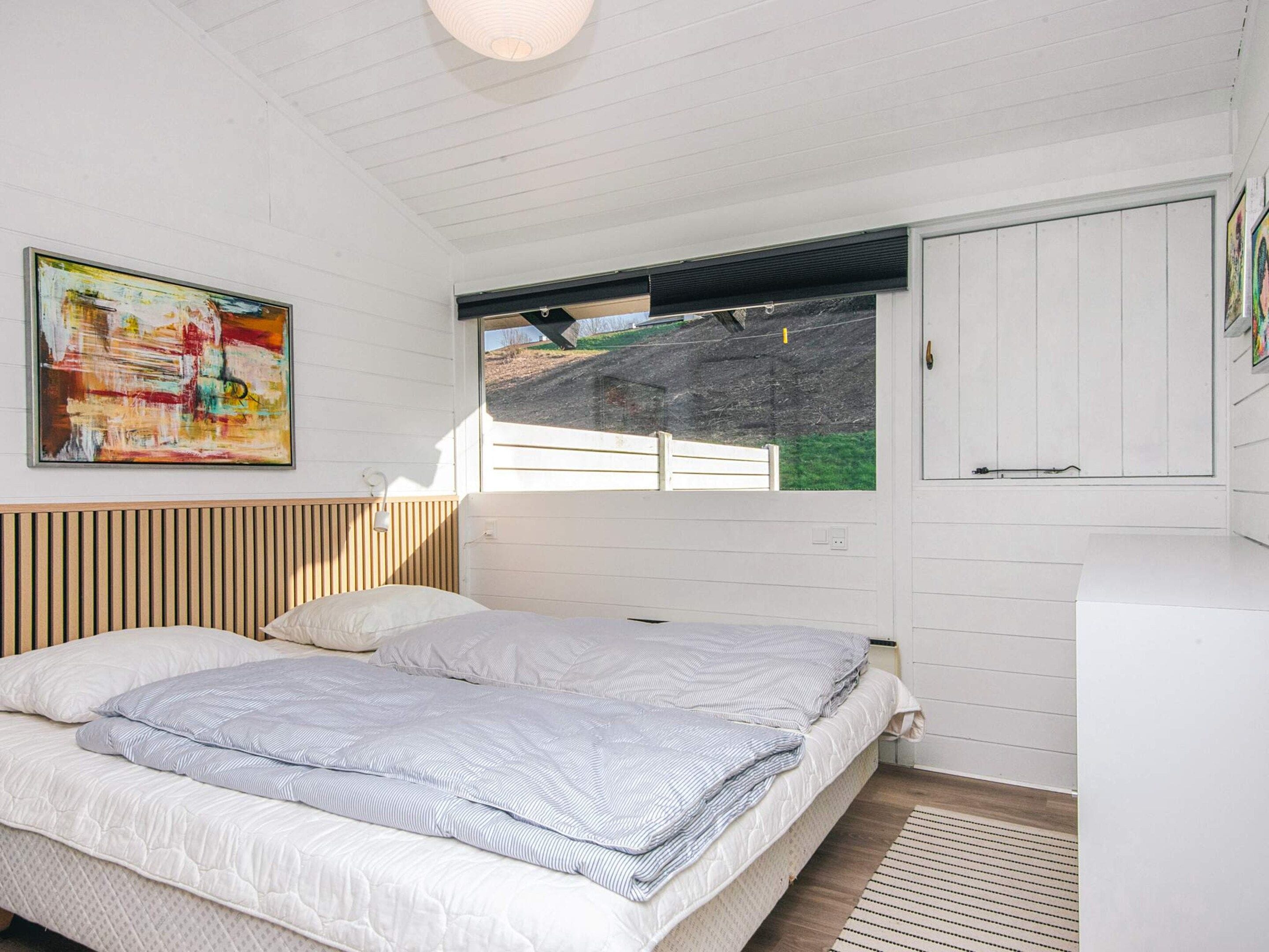Um quarto com cama, janela com vista para um gramado e um quadro na parede.