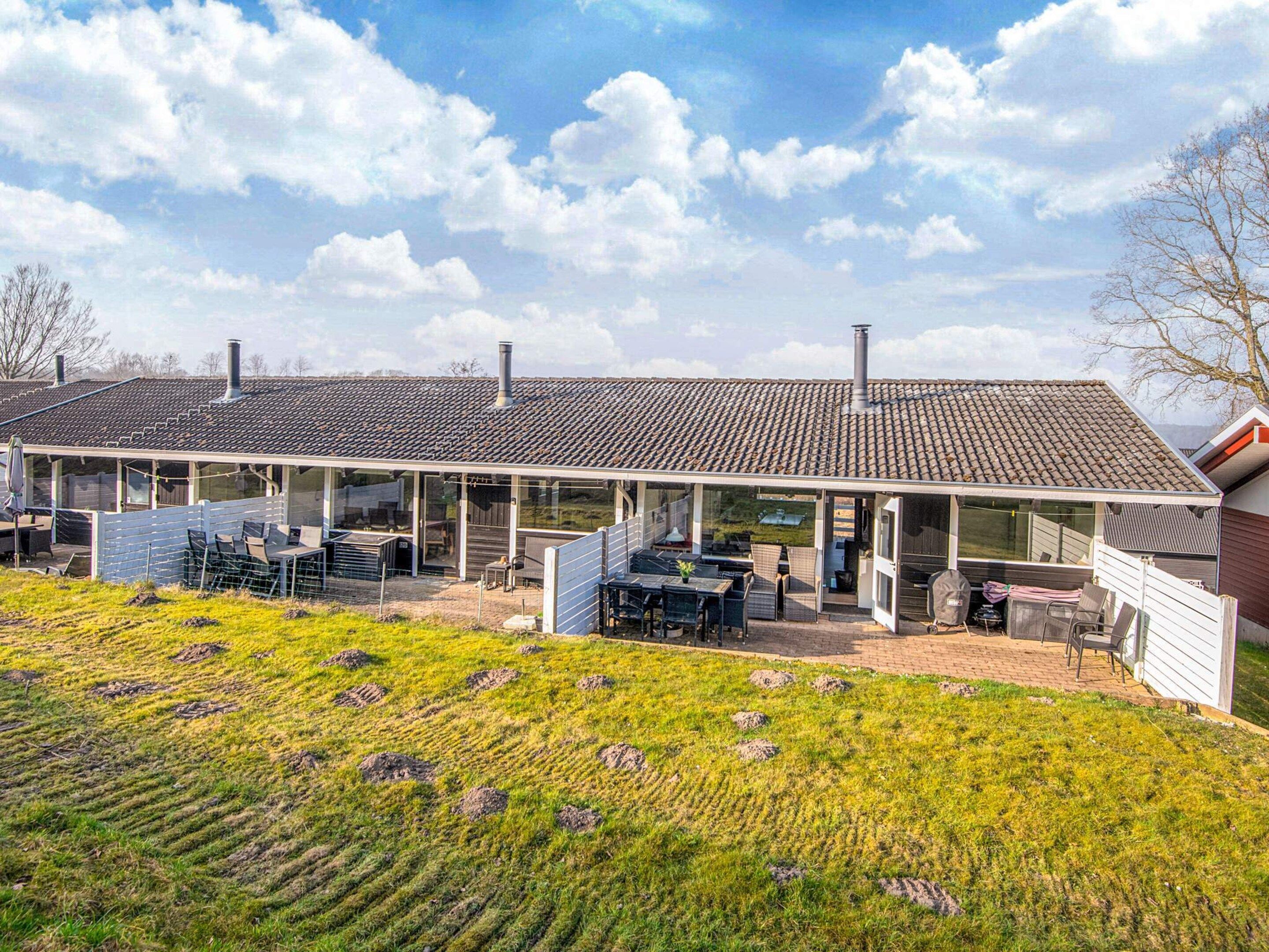 A modern building with a covered patio area, outdoor seating, and a grassy field in the foreground.