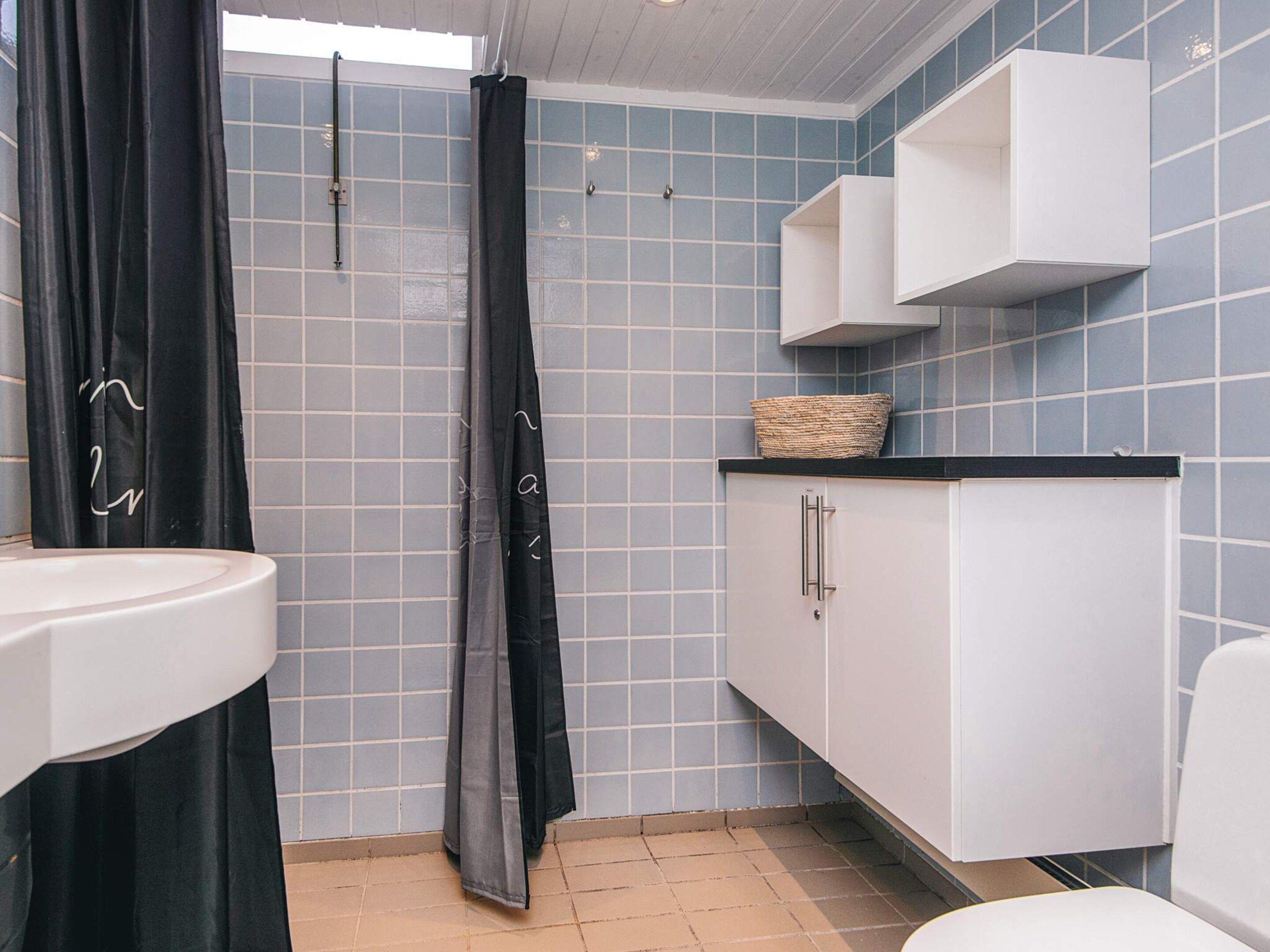 A bathroom with a white sink, a black shower curtain, a white cabinet, and a blue tiled wall.