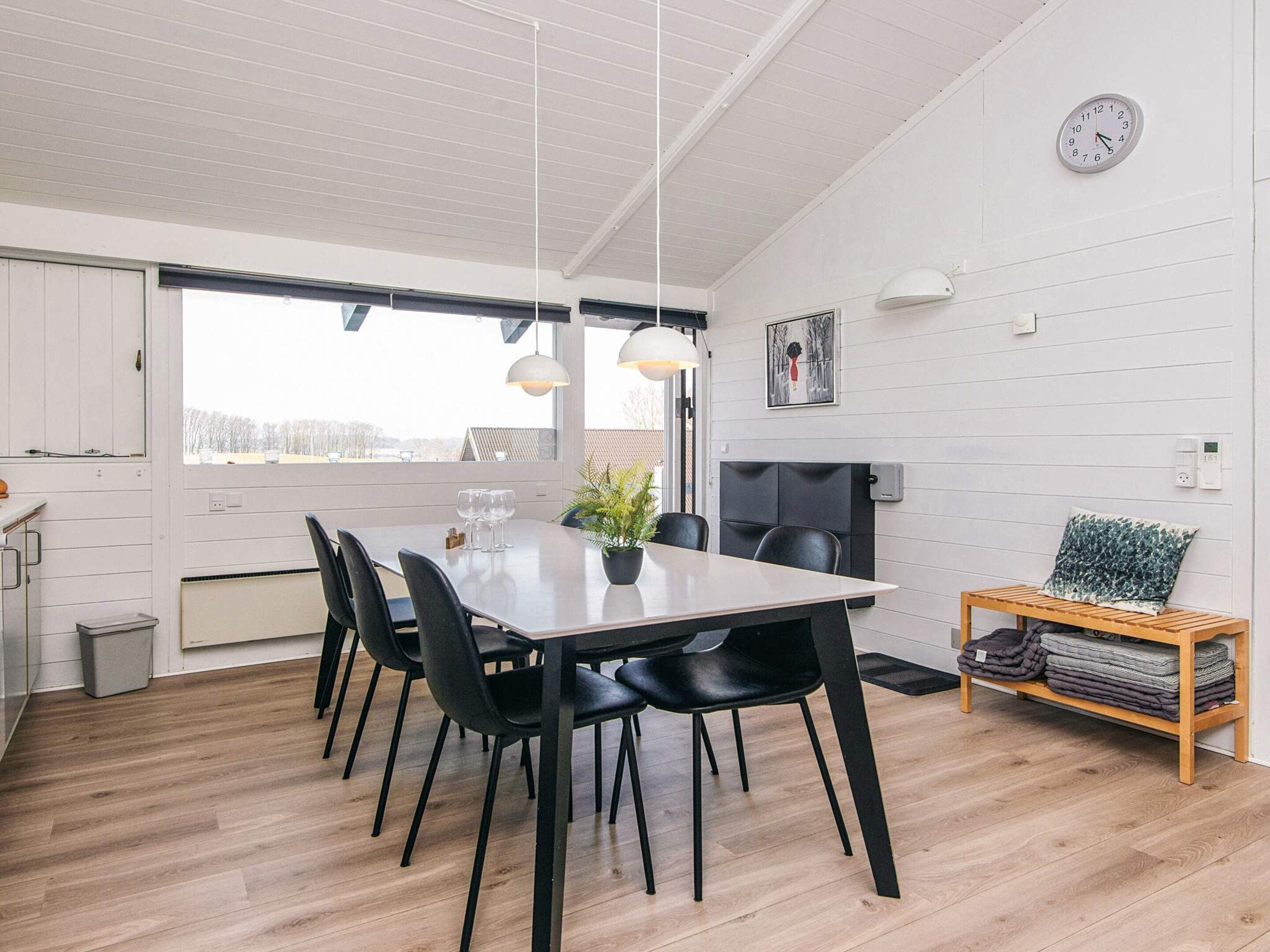 Un comedor moderno con una mesa de madera, sillas negras, lámparas colgantes y vistas a través de un ventanal.
