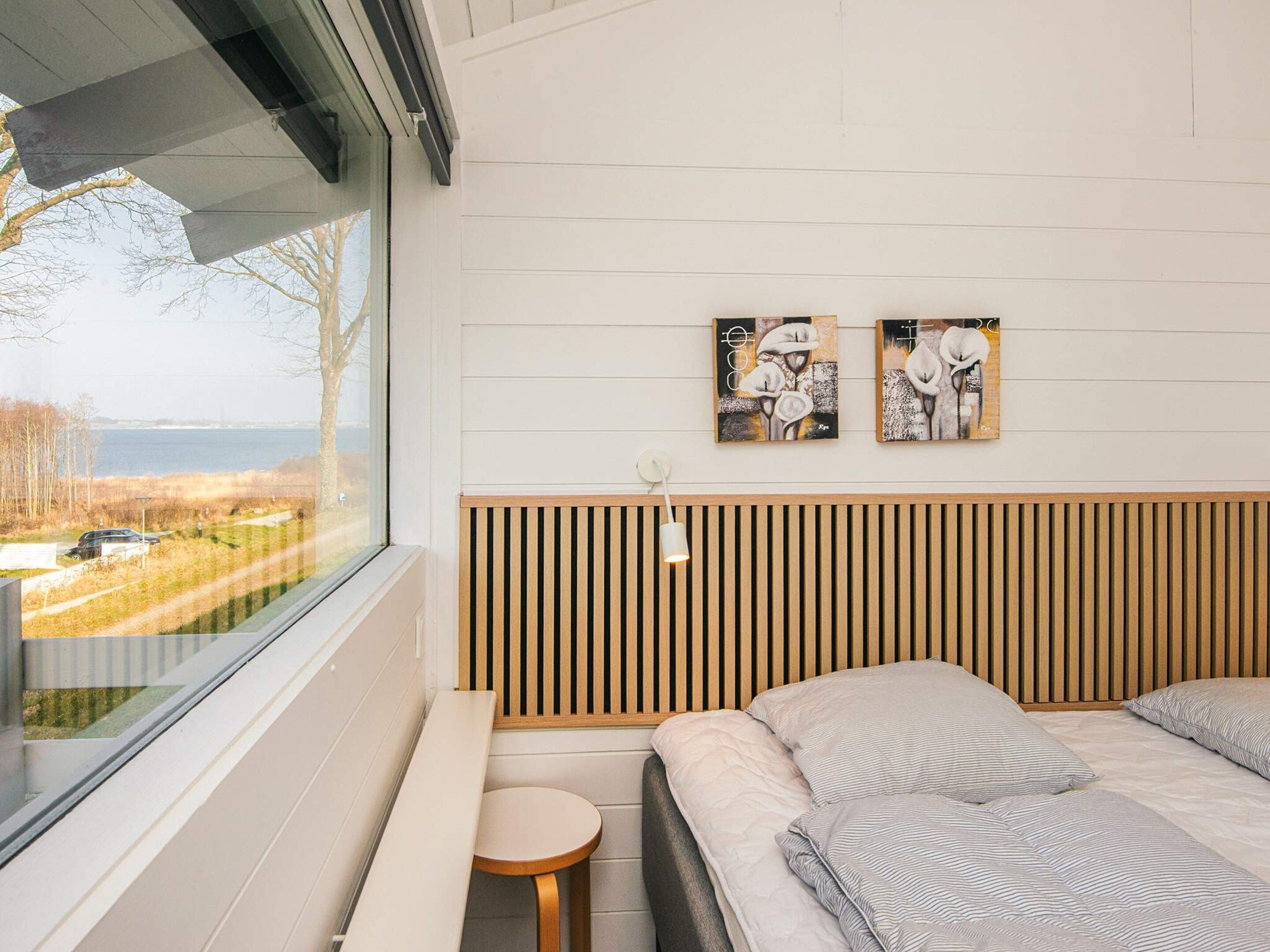 A bedroom with a large window, a bed, a small round table, and two wall-mounted paintings.