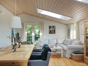 Uma sala de estar moderna com teto de madeira, uma mesa de jantar com velas, um conjunto de sofás e um quadro na parede.