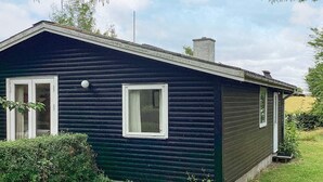 Une petite maison de couleur sombre, avec un toit à pignon, deux fenêtres et une cheminée.