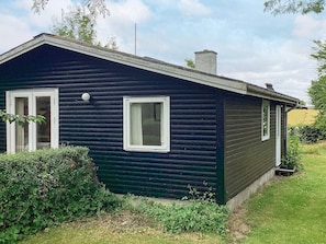 Ett litet hus med mörkfärgad fasad, ett sadeltak, två fönster och en skorsten.