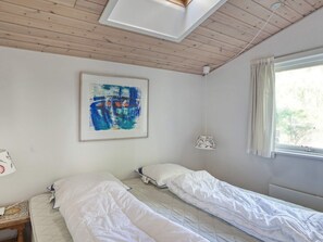 Une chambre avec deux lits, un luminaire au plafond, une fenêtre avec des rideaux et un tableau au mur.