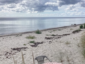 A beach with a chair and table, a clear view of the sea, and a partly cloudy sky.