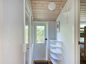 A narrow hallway with a white door, a window, and a white shelf unit.