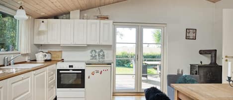 Une cuisine avec des meubles blancs, une cuisinière, un réfrigérateur et un coin repas comprenant une table et des chaises en bois.