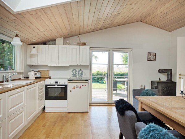 A kitchen with white cabinets, a stove, a refrigerator, and a dining area with a wooden table and chairs.