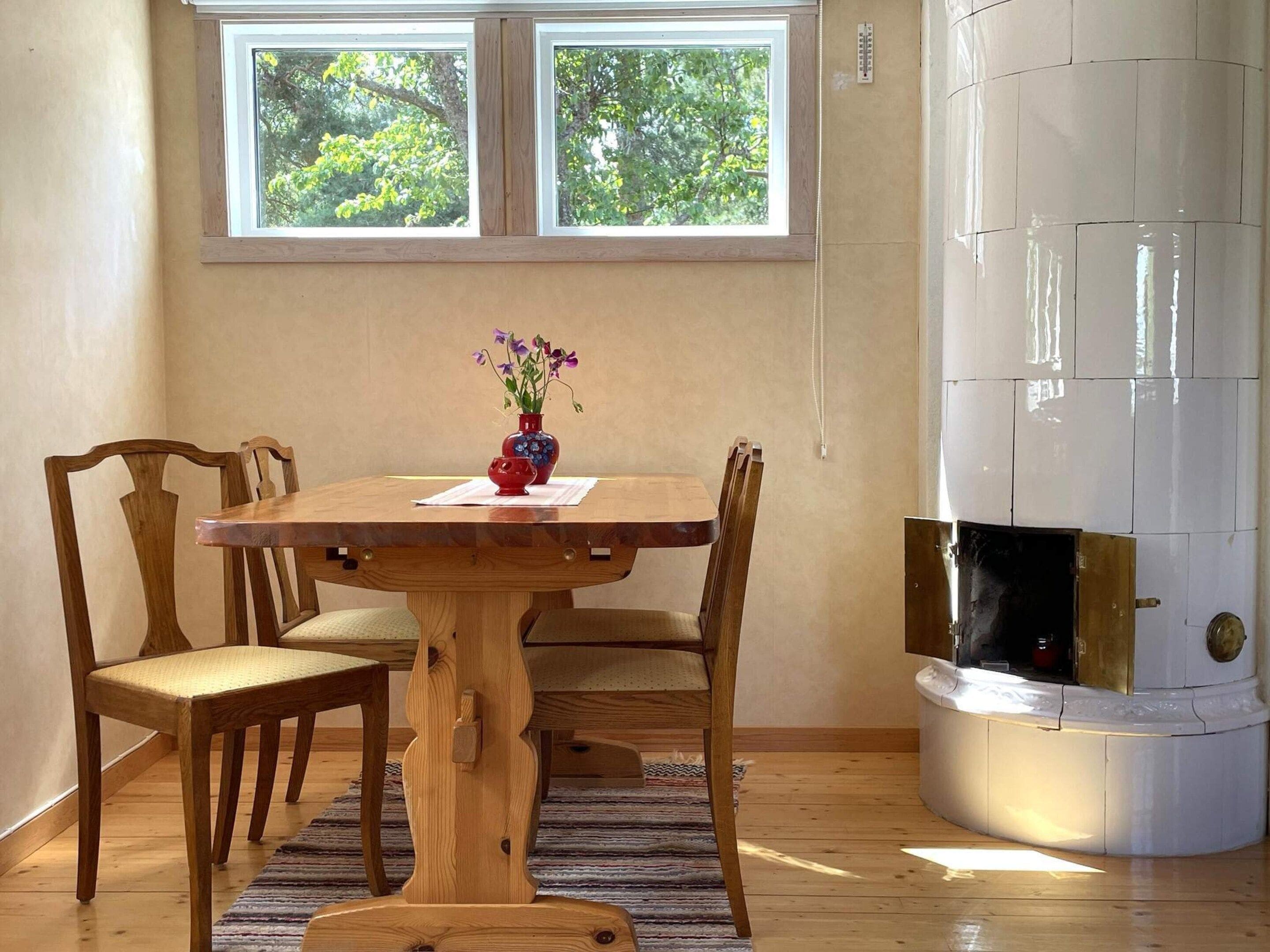 A dining area with a wooden table and chairs, a vase with flowers, and a white fireplace.