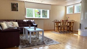 Een woonkamer met een bruine leren bank, een witte salontafel, en een eethoek met houten stoelen en een tafel.