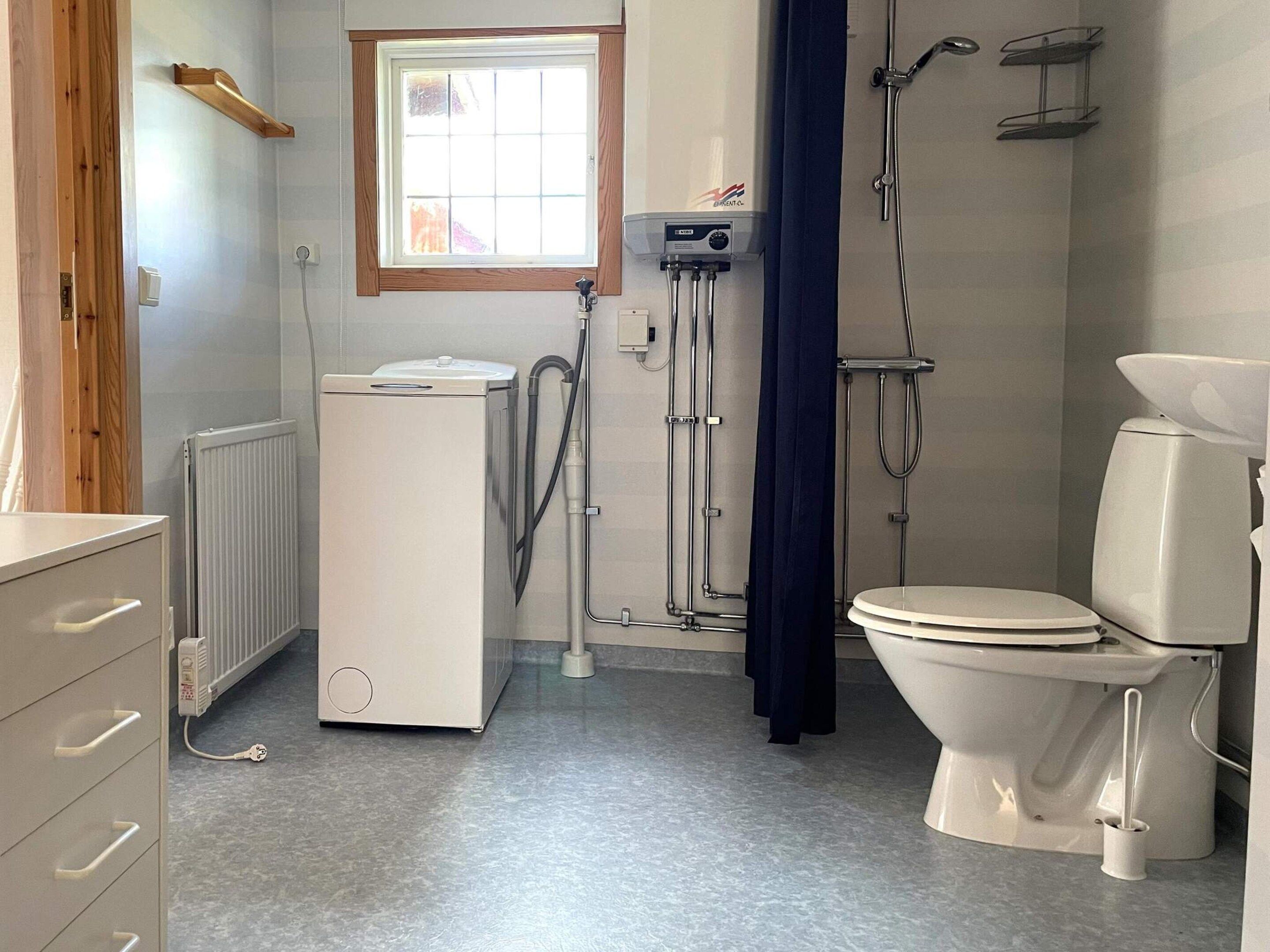 A bathroom with a toilet, a washing machine, a window, and a shower.